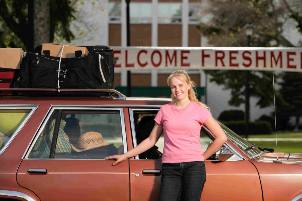 A girl stands in front of a car. Behind them is a banner reading, "Welcome Freshmen.